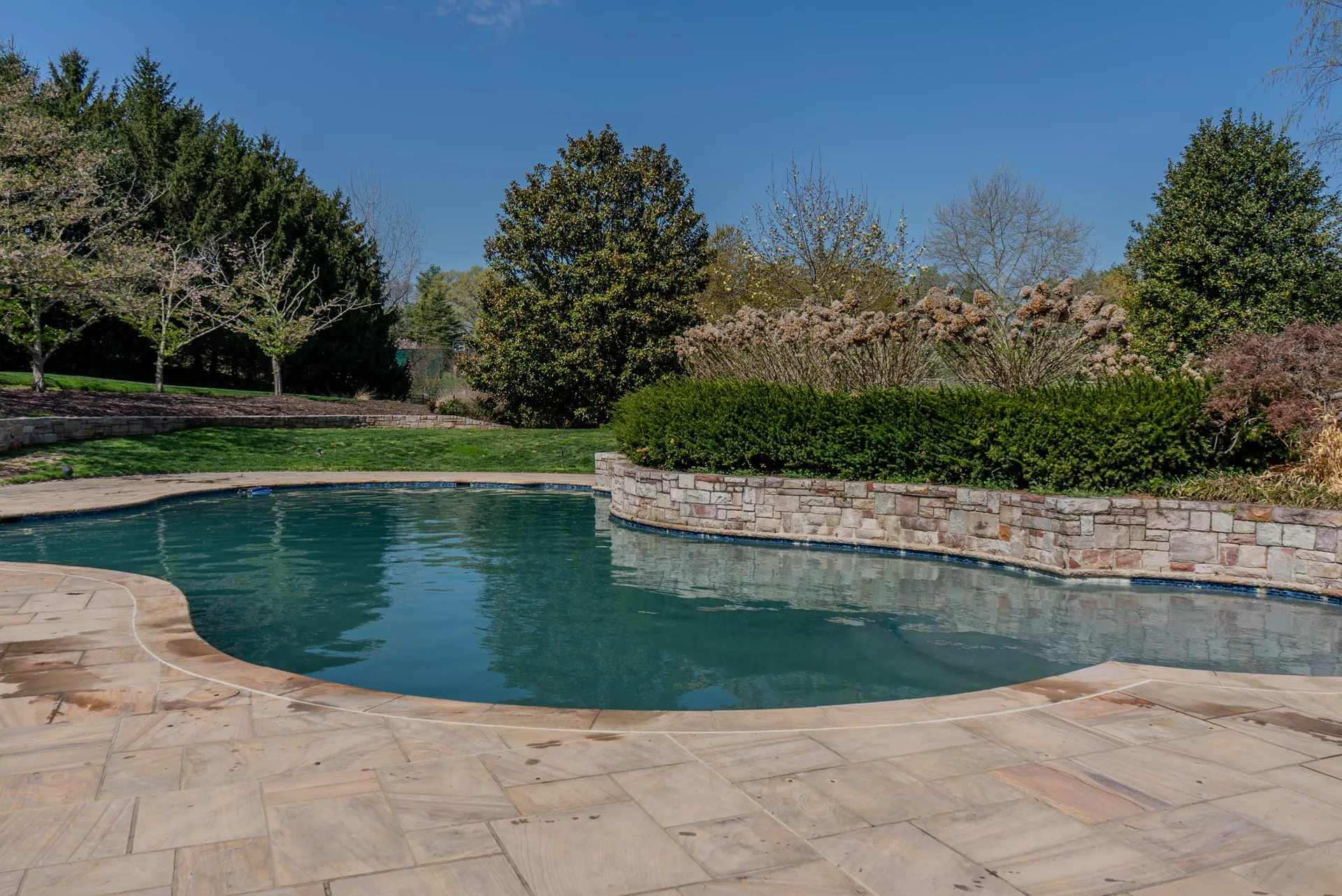 Custom freeform gunite pool with a raised stone wall and flagstone deck built by Beltway Pools