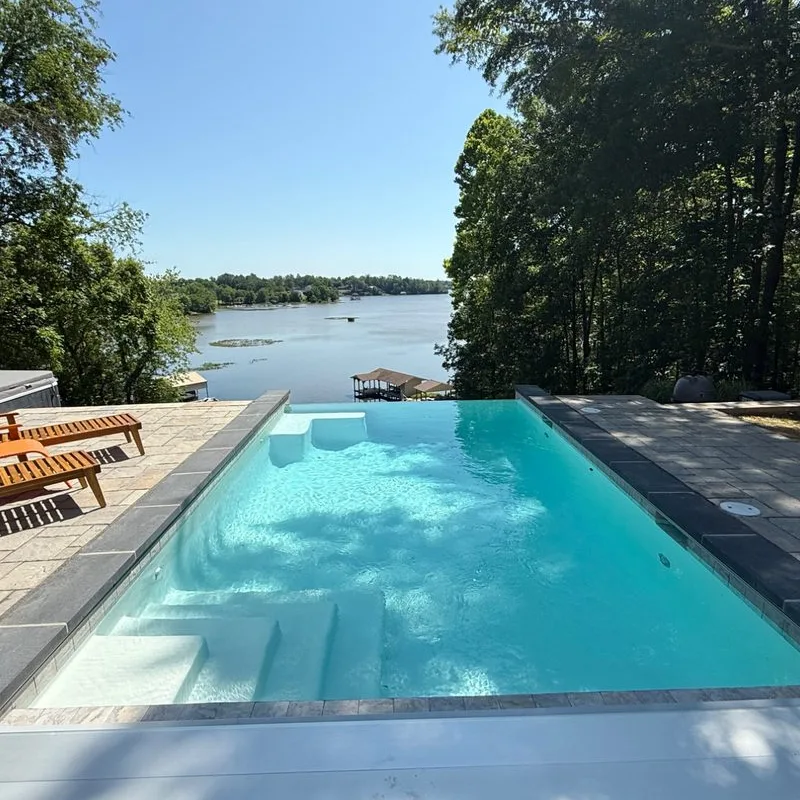 Completed Beltway Pools project: infinity-edge inground pool overlooking a lake, with a tanning ledge and paver deck
