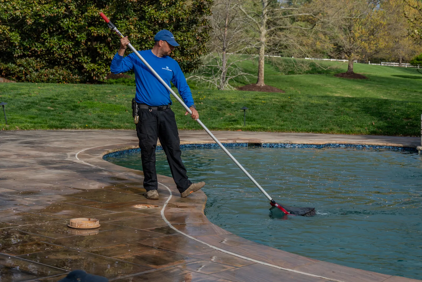 Beltway Pools technician brushing the waterline of an inground pool during a maintenance visit