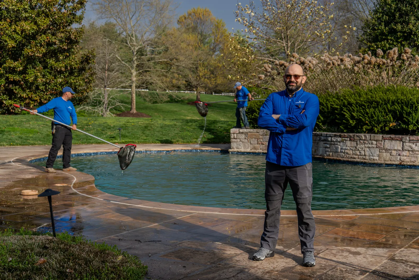 Beltway Pools maintenance technicians skimming and brushing a large freeform pool